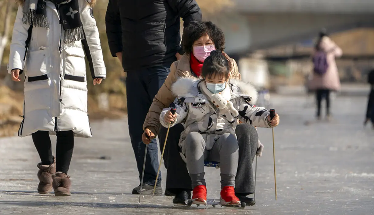 Orang-orang yang memakai masker wajah untuk melindungi dari penyebaran virus corona COVID-19 menggunakan kursi untuk meluncur melintasi permukaan kanal yang membeku di Beijing, China, Sabtu (30/1/2021). (AP Photo/Mark Schiefelbein)