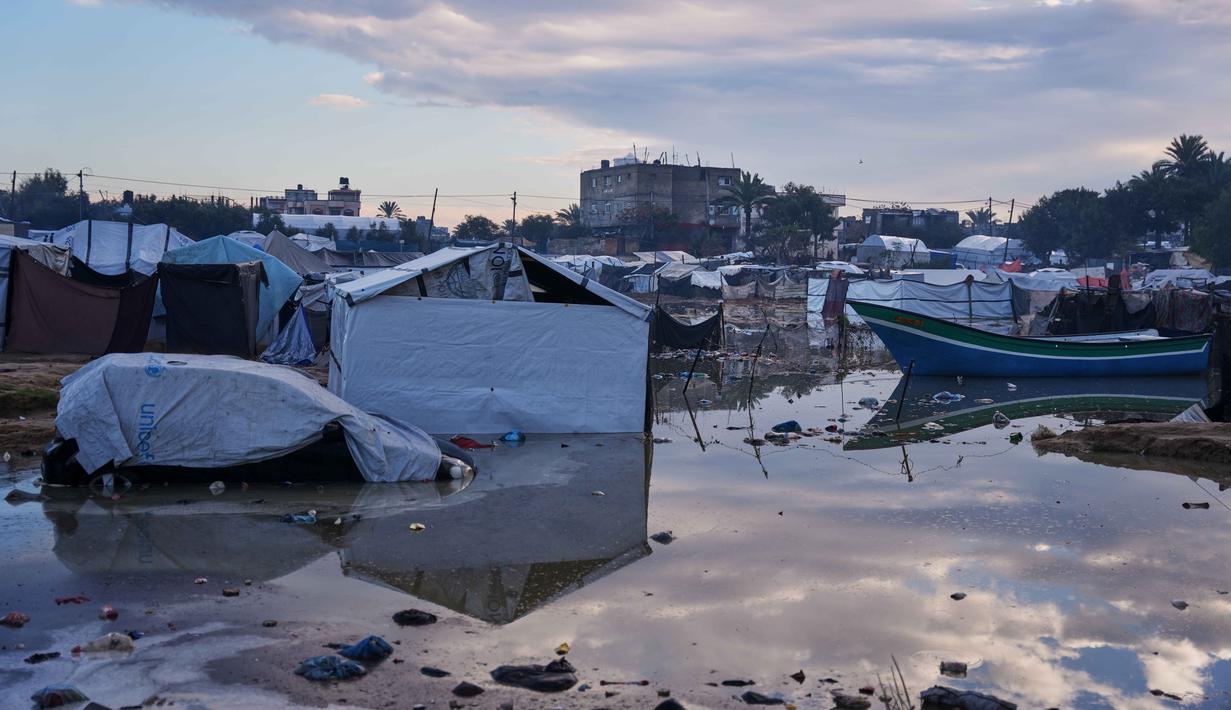 Situasi ini menambah tekanan terhadap situasi kemanusiaan meskipun gencatan senjata memasuki bulan kedua. Tampak dalam foto, sebuah mobil terlihat sebagian terendam di samping sebuah perahu kecil di daerah yang tergenang banjir setelah hujan lebat di sebuah kamp darurat untuk pengungsi Palestina, Zawaida, Jalur Gaza tengah, Rabu, 17 Desember 2025. (AP Photo/Abdel Kareem Hana)