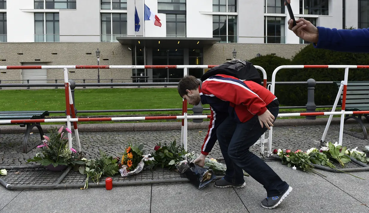 Seorang pria meletakkan bunga di luar Kedutaan Besar Perancis di Berlin, Sabtu (14/11/2015). Karangan bunga tersebut untuk menghormati para korban serangan mematikan di Paris. (AFP Photo/ Tobias Schwarz)