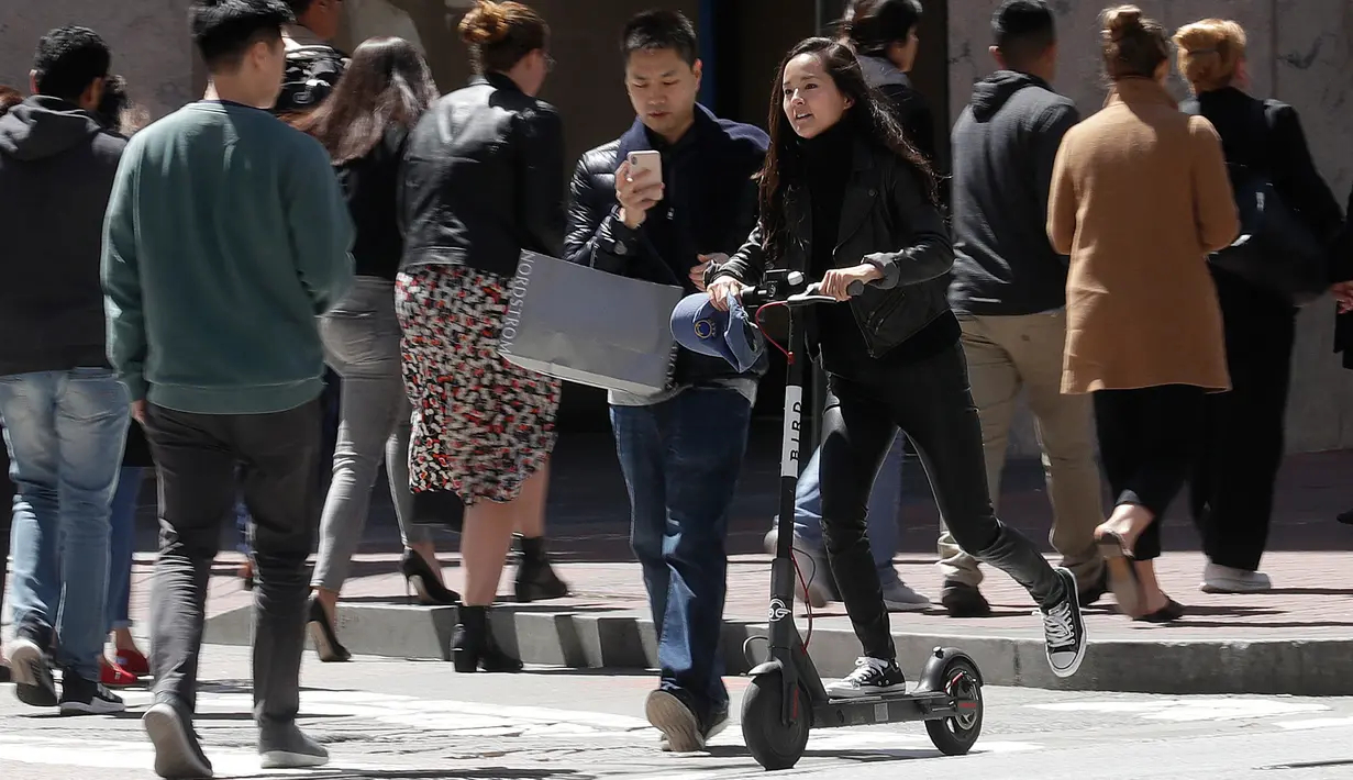 Seorang wanita menyebrang jalanan mengendarai skuter bermotor di San Francisco (17/4). San Francisco menghentikan operasi perusahaan yang menyewakan skuter bermotor. (AP/Jeff Chiu)