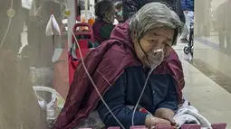 Seorang pasien lanjut usia (lansia) menerima infus saat menggunakan ventilator di lorong bangsal darurat di Beijing, Kamis (5/1/2023). Pasien, kebanyakan dari mereka lansia, berbaring di tandu di lorong dan menerima oksigen sambil duduk di kursi roda saat kasus COVID-19 melonjak di ibu kota China, Beijing. (AP Photo/Andy Wong)