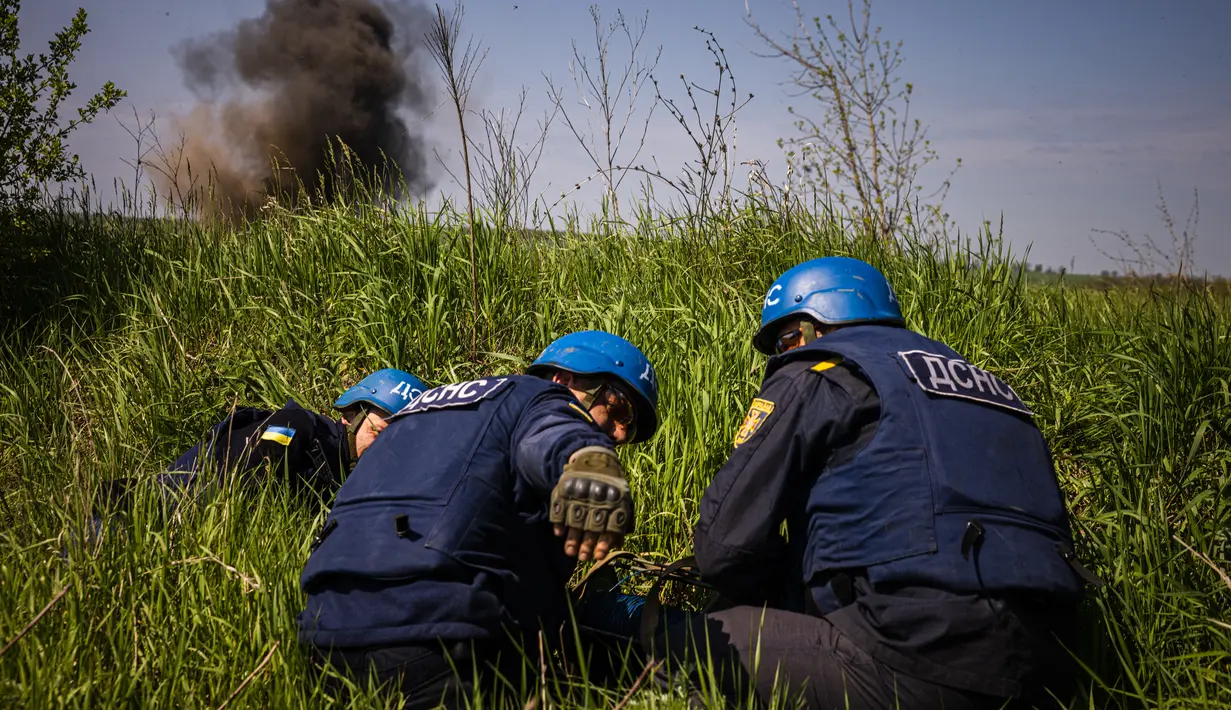 <p>Anggota tim penjinak ranjau dari Layanan Darurat Negara Ukraina berlindung selama penghancuran rudal yang belum meledak yang tersisa di dekat desa Hryhorivka, Wilayah Zaporizhzhia, di tengah invasi Rusia pada 5 Mei 2022. Musim tanam tahun ini petani membutuhkan lebih dari bahan bakar dan pupuk. Kini, mereka juga membutuhkan jaket antipeluru dan ranjau untuk menghancurkan bom yang tersebar di ladang mereka. (Dimitar DILKOFF / AFP)</p>