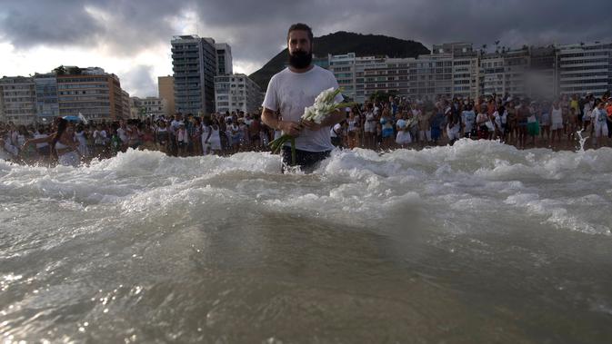 Seorang penganut kepercayaan Afro-Brasil membawa bunga sebagai persembahan untuk Dewi Laut, Yemanja dalam tradisi upacara menjelang tahun baru di pantai Copacabana, Rio de Janeiro, Sabtu (29/12). (AP/Leo Correa)