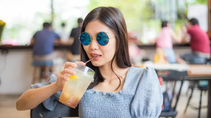 perempuan bahagia pakai kacamata minum di kafe