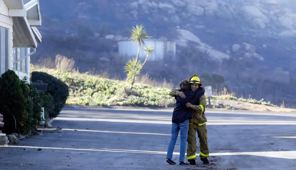 Pemadam kebakaran Simon Garcia, dari Heartland Fire Dept, mendapat pelukan dari seorang wanita setelah dia tiba untuk menemukan rumahnya masih utuh di Rancho Monserate Country Club di Fallbrook, California (8/12). (AP Photo / Gregory Bull)