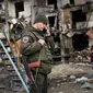 Seorang prajurit Ukraina berbicara di telepon di depan sebuah bangunan tempat tinggal yang rusak puing setelah peluru militer Rusia menghantam bangunan di Koshytsa Street, Kiev, Ukraina (25/2/2022). (AFP/Daniel Leal)