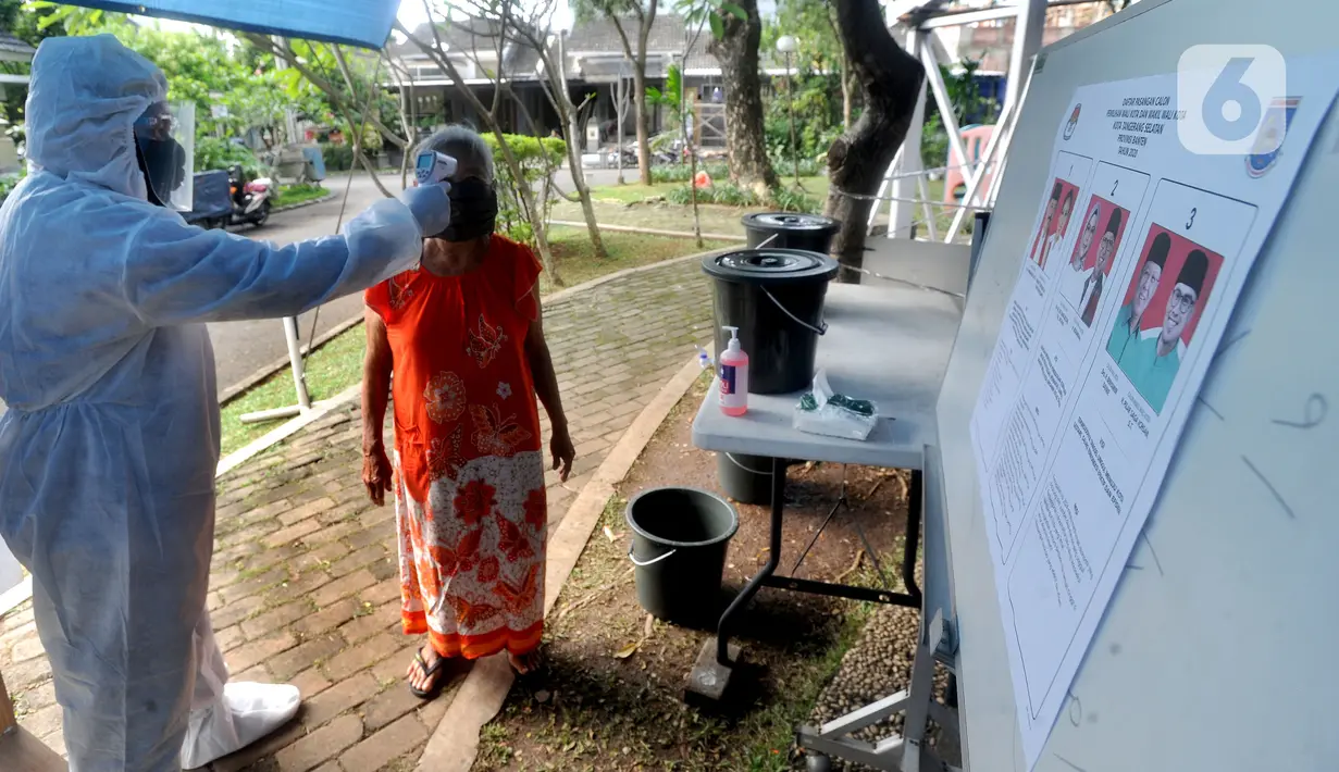 Petugas dengan memakai baju hazmat mengukur suhu warga sebelum mencoblos dalam Pilkada Tangerang Selatan 2020 di TPS 46, Paku Jaya, Serpong Utara, Rabu (9/12/2020). Para petugas KPPS di TPS 46 ini mengunakan seragam APD untuk mengantisipasi penyebaran COVID-19. (merdeka.com/Arie Basuki)