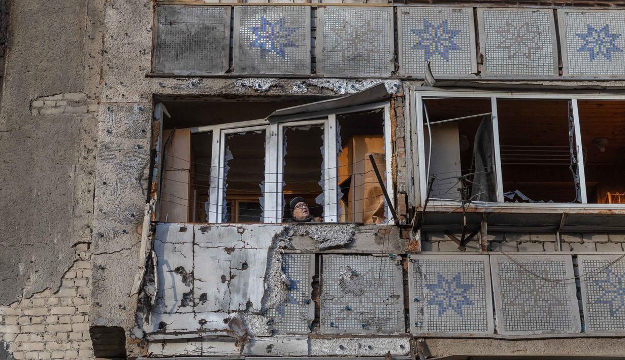 Seorang wanita berdiri di balkon sebuah bangunan tempat tinggal yang rusak akibat serangan, di Odesa, pada 31 Desember 2025, di tengah invasi Rusia di Ukraina. Jelang pergantian tahun, Rusia kembali melancarkan serangan drone yang menyasar wilayah Odesa, Ukraina, Selasa (30/12/2025) malam waktu setempat. (Oleksandr GIMANOV/AFP)