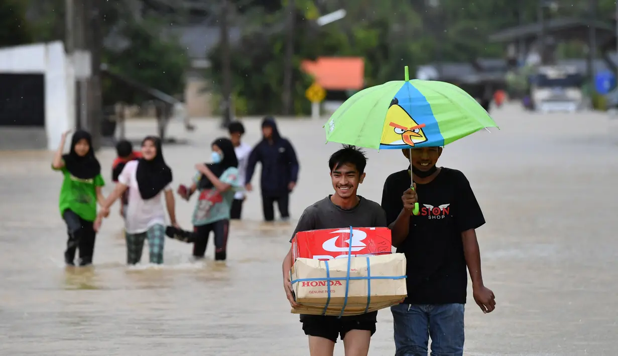 Warga berjalan melewati banjir menyusul hujan lebat di distrik Ran-ngea di provinsi Narathiwat, Thailand selatan (26/2/2022).  Hujan yang disebabkan oleh angin timur laut di atas Teluk Thailand terus berlanjut selama tiga hari berturut-turut di provinsi perbatasan selatan ini. (AFP/Madaree Tohlala)