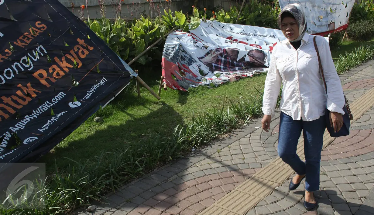 Pejalan kaki melewati Alat Peraga Kampanye (APK) yang rusak yang rusak di kawasan Ancol, Jakarta, Selasa (3/1). Alat peraga kampanye di sejumlah sudut Ibu Kota banyak yang mengalami kerusakan akibat kurangnya pengawasan. (Liputan6.com/Immanuel Antonius)