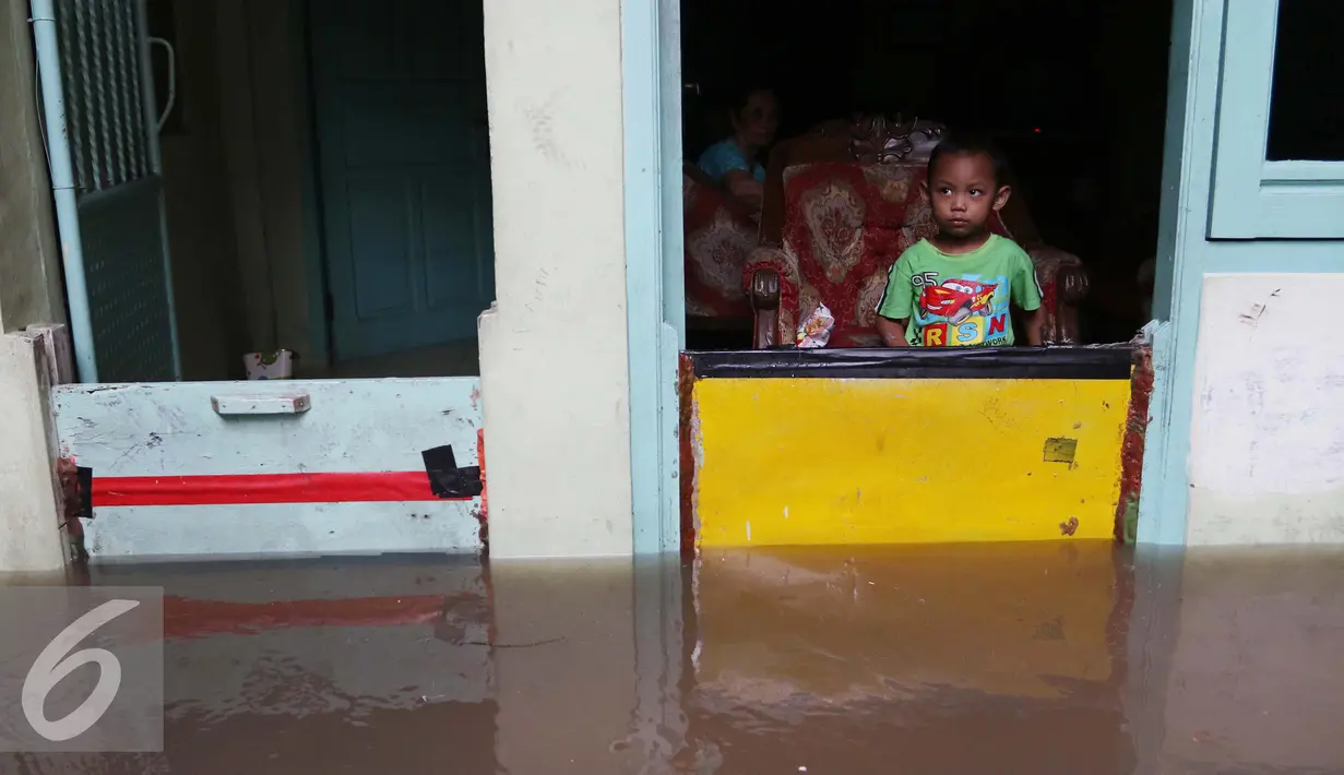 Seorang anak di dalam rumah memperhatikan banjir di kawasan Jatayu, Jakarta, Senin (21/11). Karena tingginya curah hujan serta buruknya drainase air menyebabkan meluapnya Kali Pesanggrahan yang mengakibatkan banjir. (Liputan6.com/Gempur M. Surya)