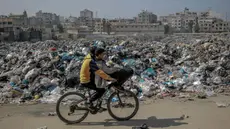 Anak-anak Palestina mengayuh sepeda melewati tempat pembuangan sampah besar di sepanjang jalan utama di Kota Gaza pada 24 Februari 2024. (Foto oleh AFP)