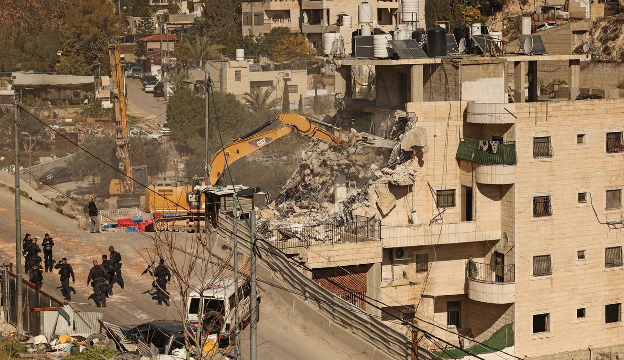Para aktivis menyebutnya sebagai pembongkaran terbesar di area tersebut tahun ini. Tampak dalam foto, pasukan keamanan Israel berkumpul saat ekskavator merobohkan sebuah bangunan yang dibangun tanpa izin di daerah Wadi Qaddum dekat lingkungan Silwan di Yerusalem timur pada Senin 22 Desember 2025. (Ahmad GHARABLI/AFP)