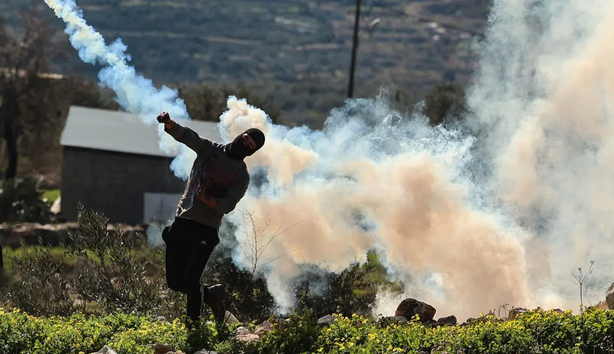 Seorang pemuda Palestina mengembalikan tabung gas air mata ke arah pasukan keamanan Israel saat bentrok pada demonstrasi menentang pengambilalihan tanah oleh Israel dekat pemukiman Yahudi Kedumim di Desa Kfar Qaddum, Tepi Barat, 21 Januari 2022. (JAAFAR ASHTIYEH/AFP)