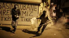 Dua militan Kurdi bersiap melemparkan tabung gas air mata ke arah polisi anti huru hara Turki dalam bentrokan di distrik Okmeydani, Istanbul (15/12/2015). Bentrokan terjadi karena pemerintah memberlakukan pembatasan jam malam. (AFP Photo/ Cagdas Erdogan)