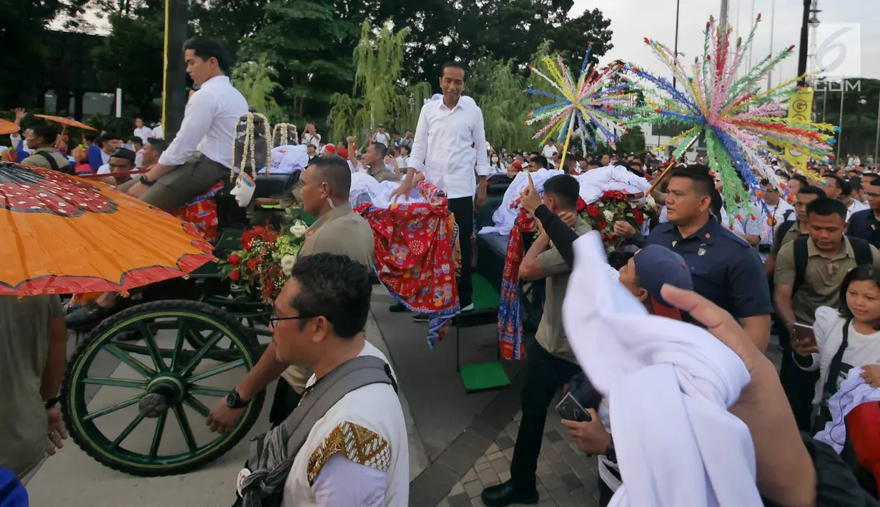 Capres 01 Joko Widodo didampingi Iriana Jokowi dan Kaesang Pangarep melempar kaus seusai 'Konser Putih Bersatu' di Stadion GBK, Jakarta, Sabtu (13/4). Pasangan Capres dan Cawapres 01 menggunakan kereta kencana seusai Konser Putih Bersatu menuju lokasi debat. (Liputan6.com/Herman Zakharia)