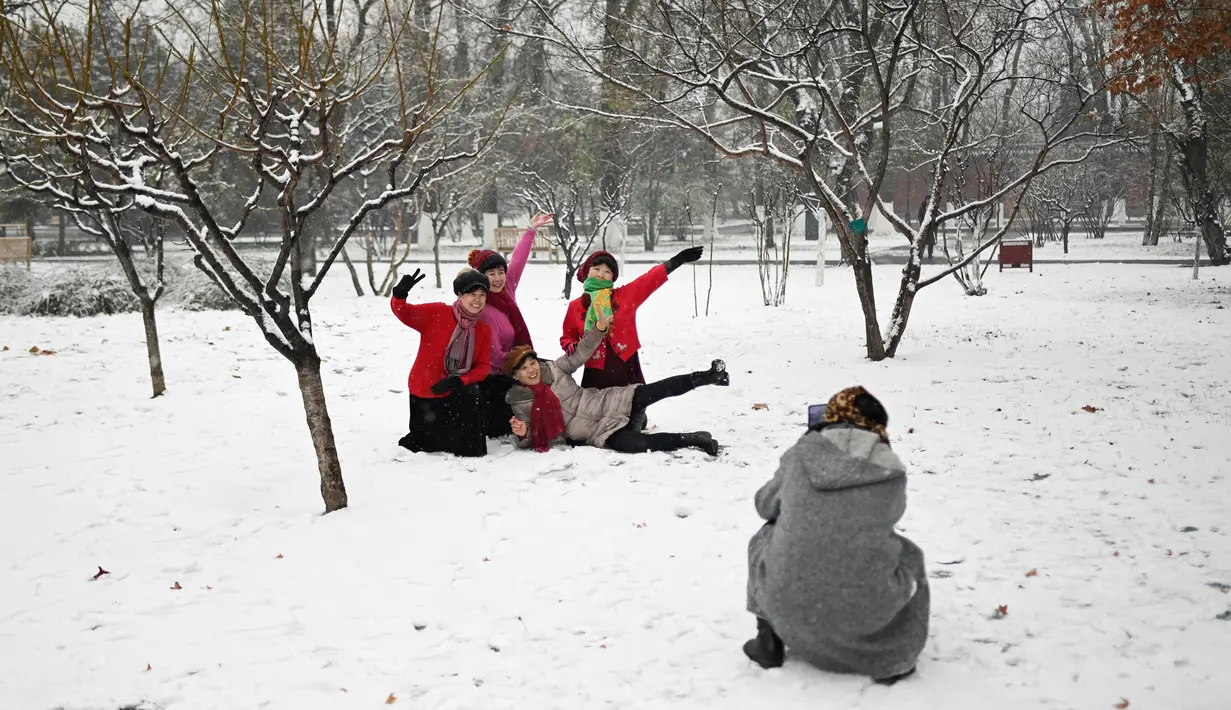 Sejumlah wanita berpose saat salju turun di sebuah taman di Beijing (16/12/2019). Pada pukul 7 Senin pagi, 42 penerbangan telah dibatalkan di Bandara Internasional Ibukota Beijing. (AFP Photo/Wang Zhao)