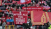Penggemar Liverpool memegang poster yang mengejek skandal keuangan Manchester City saat kru televisi bekerja di tepi lapangan menjelang pertandingan Liga Inggris antara Liverpool dan Manchester City di Anfield di Liverpool, barat laut Inggris pada 11 Oktober 2026. Manchester City menghadapi Anfield yang bermusuhan pada hari Minggu ketika pemimpin Premier League itu menghadapi rival sengitnya Liverpool dalam pertandingan pertama mereka sejak dinyatakan bersalah karena melanggar lebih dari 100 aturan keuangan. (Paul ELLIS/AFP)
