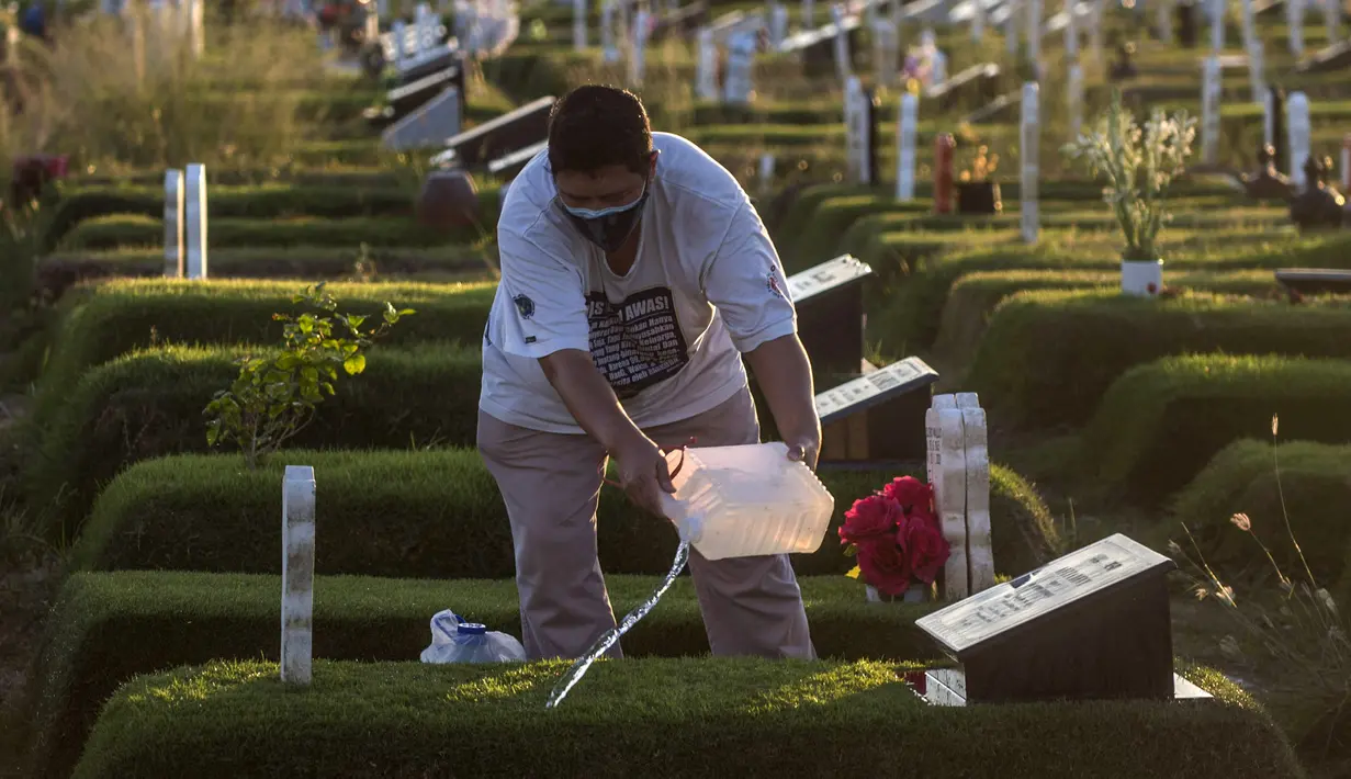 Seorang pria menyiramkan air ke makam kerabatnya di lokasi pemakaman korban virus corona COVID-19 di TPU Keputih, Surabaya, Jawa Timur, Sabtu (17/7/2021). Di Kota Surabaya terdapat dua tempat lahan pemakaman khusus blok COVID-19 yakni TPU Keputih dan TPU Babat Jerawat. (JUNI KRISWANTO/AFP)