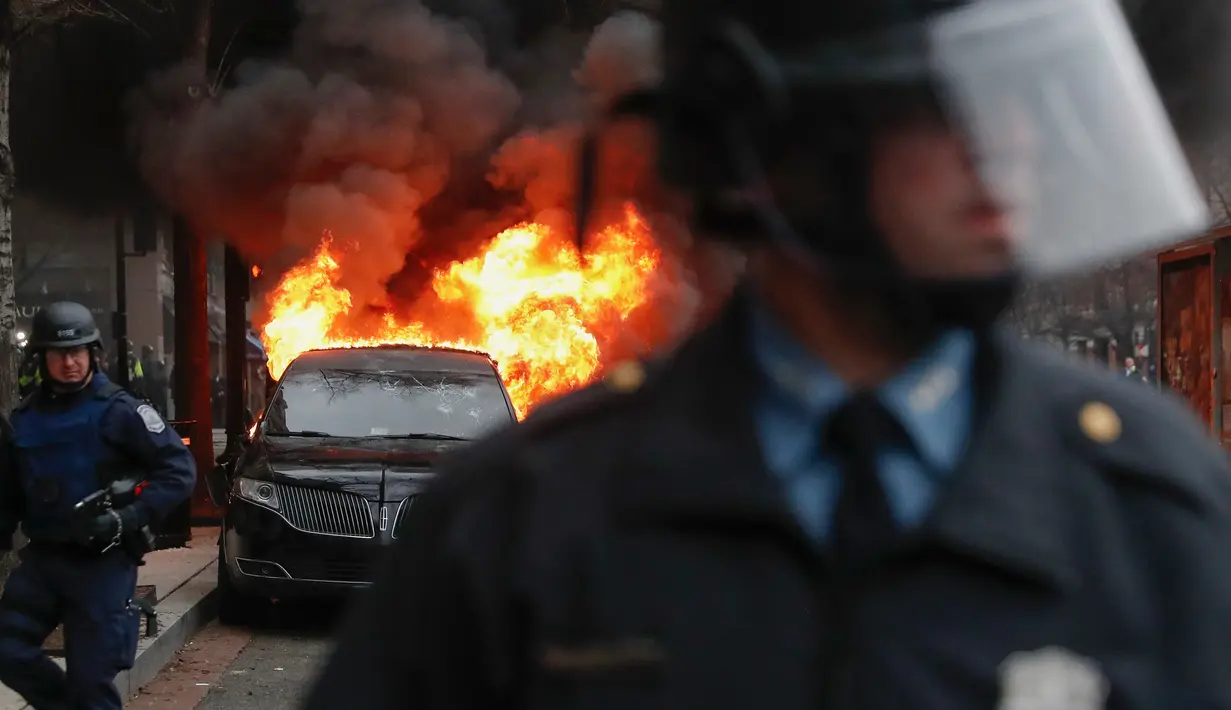 Aparat kepolisian berjaga di dekat sebuah limusin yang dibakar dalam aksi protes warga saat berlangsungnya upacara pelantikan Donald Trump menjadi Presiden Amerika Serikat yang ke-45 di Washington, DC, AS, (20/1). (AP Photo/John Minchillo)