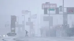 Seorang pria menyebrang jalan di bawah salju lebat saat terjadi badai salju di Jersey City, New Jersey (21/3). New Jersey telah mengumumkan keadaan darurat di mana sejumlah sekolah di Philadelphia ditutup. (AP/Julio Cortez)