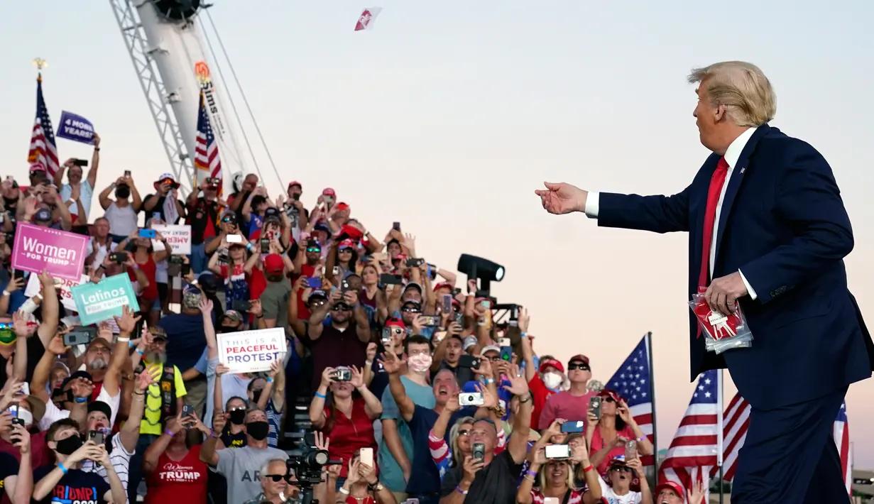 Presiden Donald Trump melemparkan masker dari atas panggung ke kerumunan pendukung saat berkampanye di Bandara Internasional Orlando Sanford di Sanford, Florida, Senin (12/10/2020). Donald Trump kembali berkampanye untuk pertama kalinya usai dinyatakan negatif Covid-19. (AP Photo/Evan Vucci)