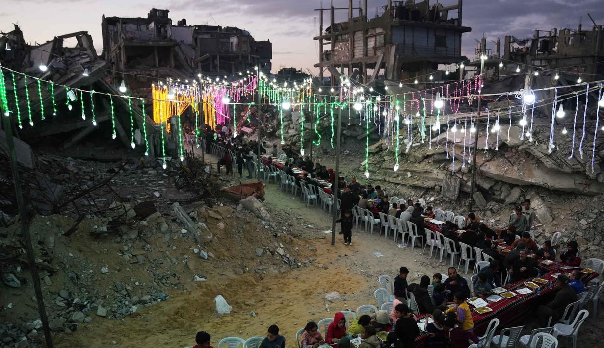Lentera ini menjadi simbol ketahanan dan harapan di tengah gelapnya wilayah akibat krisis listrik. Tampa dalam foto, warga Palestina duduk di meja panjang di tengah reruntuhan bangunan yang hancur untuk berbuka puasa bersama, selama bulan suci Ramadan di Khan Younis, Jalur Gaza, Kamis 19 Februari 2026. (AP Photo/Abdel Kareem Hana)