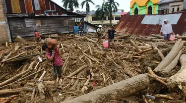 Orang-orang berjalan di atas puing-puing di daerah yang terkena banjir bandang di Masamba, Sulawesi Selatan, Rabu (15/7/2020). Banjir bandang akibat tingginya curah hujan tersebut mengakibatkan 16 orang meninggal dunia dan puluhan warga dilaporkan masih dalam pencarian. (AP/Khaizuran Muchtamir)