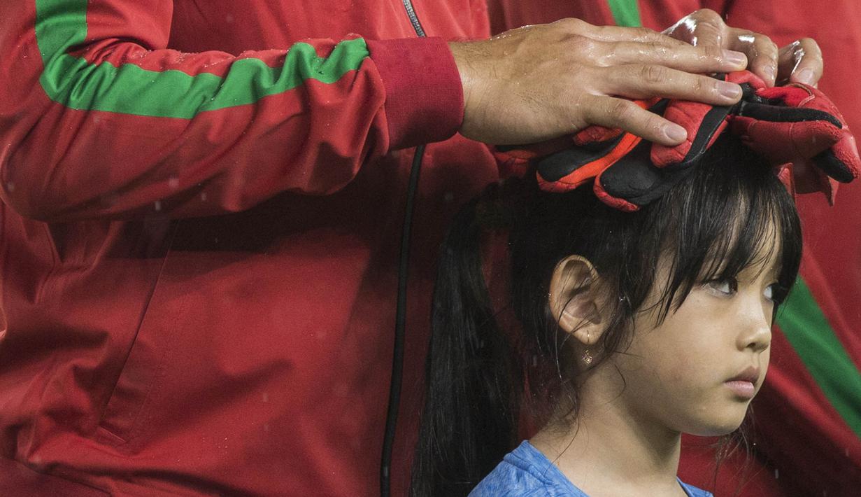 Kiper Timnas Indonesia, Andritany Ardhiyasa, melindungi seorang anak dari hujan saat akan melawan Islandia pada laga persahabatan di SUGBK, Jakarta, Minggu (14/1/2018). Timnas Indonesia kalah 1-4 dari Islandia. (Bola.com/Vitalis Yogi Trisna)