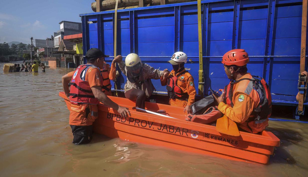 Banjir yang melanda sejumlah titik di Kabupaten Bandung juga menyebabkan 162 kepala keluarga (KK) atau sekitar 457 jiwa harus dievakuasi ke tempat pengungsian. Tampak dalam foto, tim penyelamat membantu seorang perempuan yang terjebak banjir di samping truk pengangkut kayu di Bandung, Jawa Barat, pada Jumat 5 Desember 2025. (TIMUR MATAHARI/AFP)