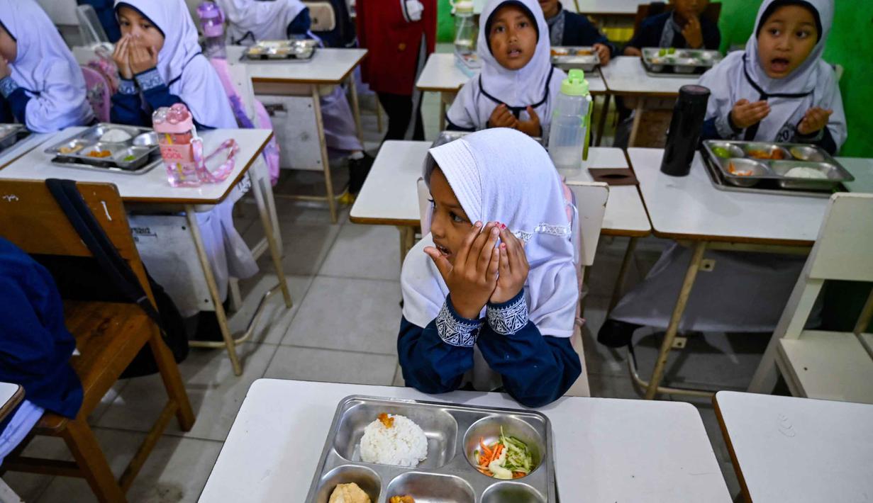 Para siswa berdoa sebelum menyantap makanan yang dipasok oleh program Makan Bergizi Gratis (MBG) di sebuah sekolah dasar, Banda Aceh pada Kamis 30 Oktober 2025. Sejak awal tahun 2025, program Makan Bergizi Gratis (MBG) di Banda Aceh diketahui telah berjalan baik. (CHAIDEER MAHYUDDIN/AFP)