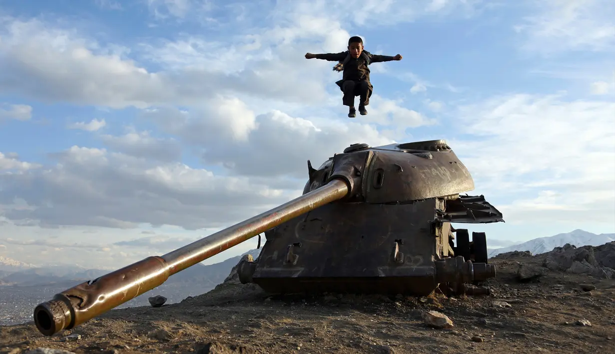 Seorang anak melompat di atas bangkai tank Soviet di puncak bukit di pinggiran Kabul, Afghanistan (4/3). Karena Afghanistan negara yang dilanda konflik, banyak barang-barang sisa perang yang dibiarkan begitu saja. (AP Photo/Rahmat Gul)
