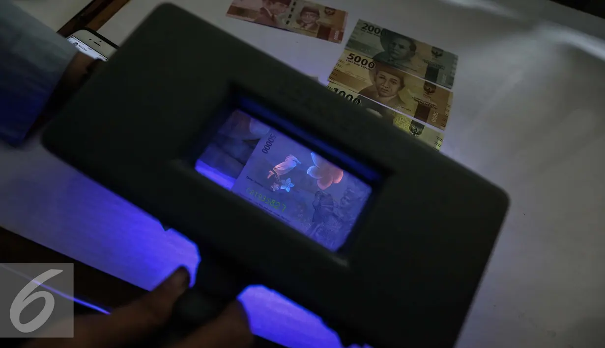 Petugas menunjukan alat untuk melihat gambar yang tersembunyi di uang kertas rupiah di kantor Peruri, Karawang, Jawa Barat, Rabu (18/1). (Liputan6.com/Faizal Fanani)
