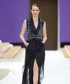 Potret busana Chanel Haute Couture Spring/Summer 2022 berikut bisa dijadikan inspirasi model baju pesta yang elegan dan mewah. Gaun warna hitam dengan detail bukaan di bagian depan ini dipadukan vest chanel berbahan tweed. Stylish dan catchy! (Dok/Chanel).