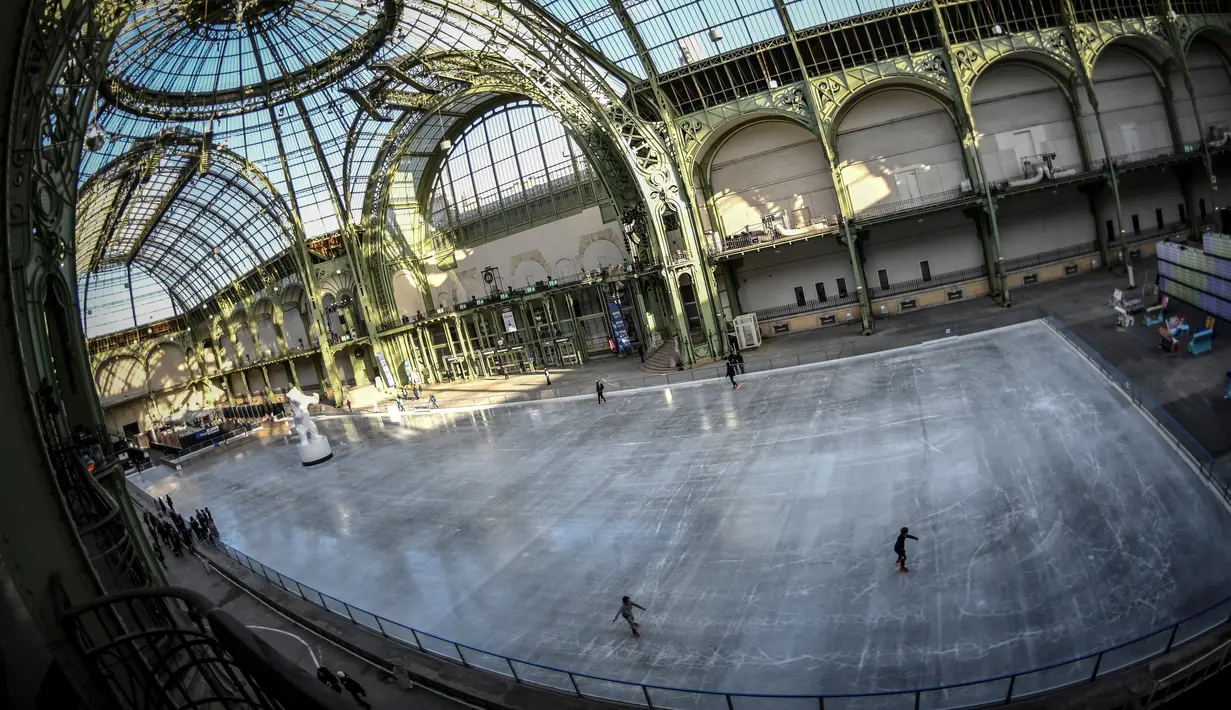 Orang-orang  berseluncur di arena ice skating di bawah kubah kaca mewah legendaris, Grand Palais, Paris, Senin (17/12). Tempat seluas 1.800 meter persegi ini menjadi arena ice skating sementara terbesar di Prancis. (STEPHANE DE SAKUTIN / AFP)