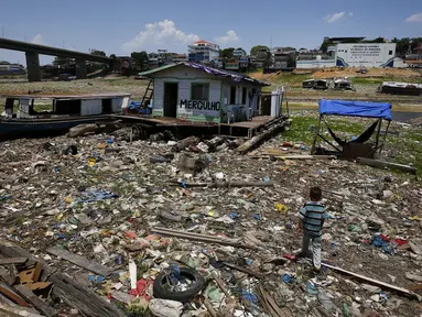 Anak laki-laki berjalan di samping rumah terapung yang terdampar di tempat yang dulunya merupakan tepi sungai Negro, di tengah kekeringan di Manaus, Brasil, Selasa, 26 September 2023. (AP Photo/Edmar Barros)