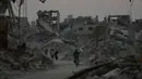 Penghalangan akses dan birokrasi ini jelas menghambat proses pemulihan dan memperpanjang penderitaan warga sipil Gaza. Tampak dalam foto, pengungsi Palestina berjalan di antara reruntuhan bangunan yang hancur di Khan Younis, Jalur Gaza, Sabtu 8 November 2025. (AP Photo/Abdel Kareem Hana)
