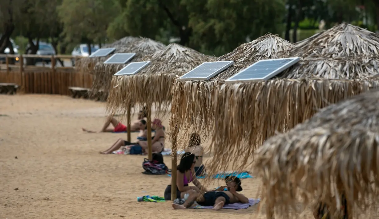 Panel surya terpasang pada sejumlah payung di pantai dekat Balai Kota Vari-Voula-Vouliagmeni, Yunani, Selasa (21/7/2020). Puluhan payung di sepanjang pantai tersebut dilengkapi sistem panel surya dan port USB untuk menyediakan pengisian daya gratis dan ramah lingkungan. (Xinhua/Lefteris Partsalis)