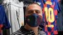 Fans memakai masker berlogo Barcelona di Toko Asesoris Barcelona, Senin (25/5/2020). Di tengah pandemi virus Corona, Barcelona menjual masker dengan harga 18 euro atau sekitar Rp 291 ribu. (AFP/Lluis Gene)