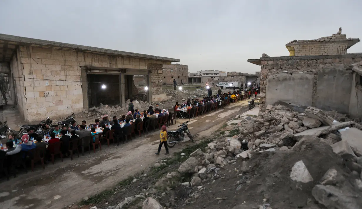Warga Suriah berkumpul di daerah yang rusak berat untuk berbuka puasa di Tadef, dekat kota perbatasan al-Bab, yang dikendalikan pemberontak yang didukung Turki di Suriah (18/4/2022). Buka puasa ini diselenggarakan oleh sebuah LSM berkoordinasi dengan berbagai faksi lokal. (AFP/Bakr Alkasem)