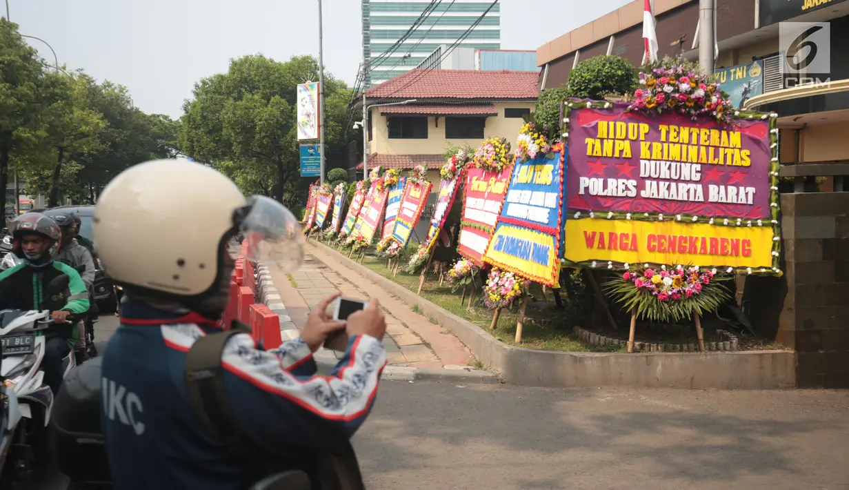 Warga mengabadikan karangan bunga di Halaman Polres Jakarta Barat, Jumat (23/11). Puluhan karangan bunga yang dikirimkan warga tersebut diberikan guna mendukung kepolisian dalam memberantas aksi premanisme di Jakarta Barat. (Liputan6.com/Faizal Fanani)