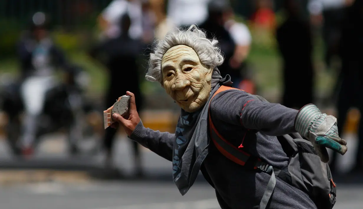 Seorang pengunjuk rasa memakai topeng, bersiap melempar batu saat mereka bentrok dengan polisi antihuru-hara menuntut Presiden Venezuela, Nicolas Maduro di Caracas (10/7). (AP Photo/Ariana Cubillos)