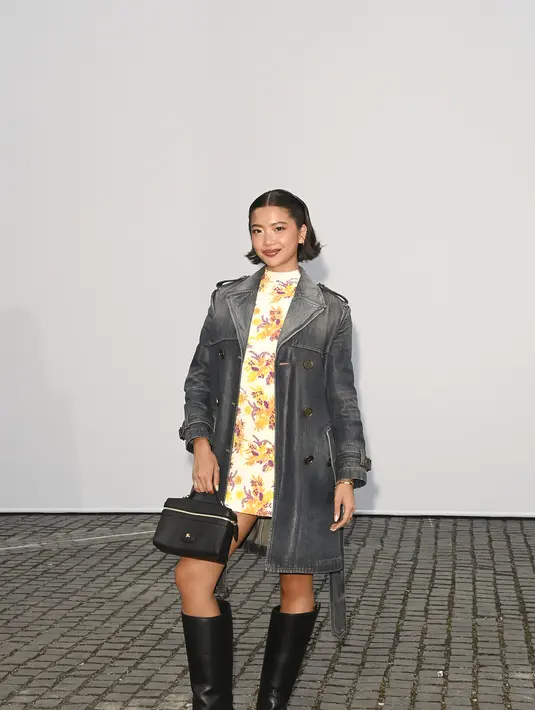 Stephanie Hui memilih trench coat denim abu-abu yang dikenakan terbuka, menampilkan dress motif bunga kuning-ungu di dalamnya, dilengkapi boots tinggi hitam [dok. Burberry]