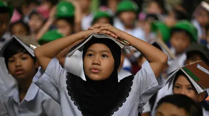 Para pelajar muda meletakkan buku di kepala mereka saat berkumpul di pusat evakuasi yang telah ditentukan di luar gedung sekolah selama latihan gempa bumi di salah satu sekolah dasar di Manila, Filipina pada 11 September 2025. (Ted ALJIBE/AFP)
