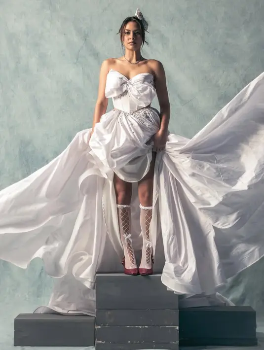 Gaun putih tersebut memiliki model rok pendek di bagian depan dan flowy panjang di bagian belakang. Melengkapinya dengan kaos kaki putih sheer cut out depan berpita dan renda. [@valerieethomas]