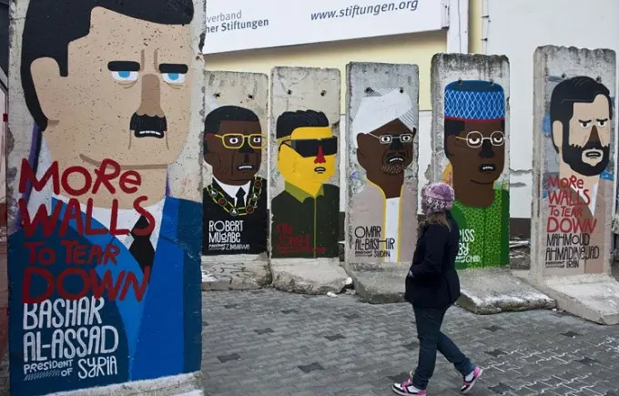 Seorang gadis melihat-lihat bekas Tembok Berlin yang digambari dengan karikatur para pemimpin dunia. Graffiti itu dilukis oleh artis Prancis Guillaume Kashima, dekat Checkpoint Charlie di Berlin, Jerman, 13 Januari 2013. (John MacDougall/AFP)