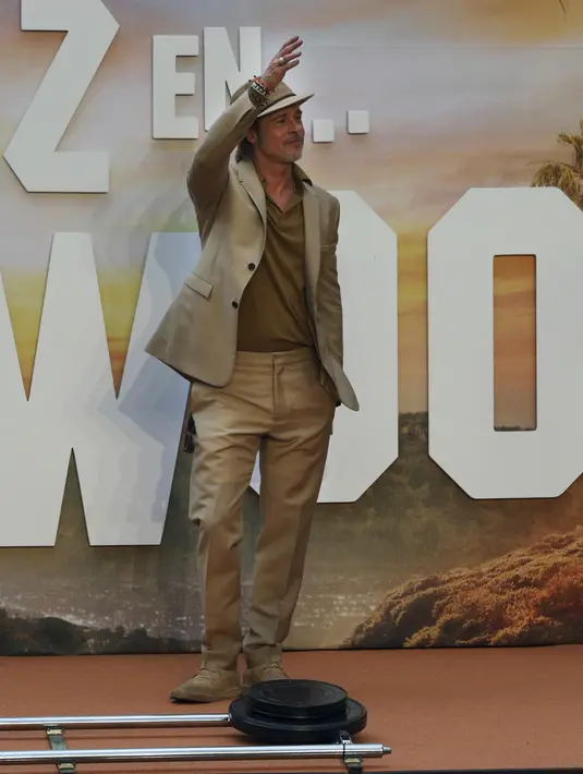 Brad Pitt menyapa penggemar saat menghadiri acara karpet merah untuk film "Once Upon a Time In Hollywood" di Mexico City (12/8/2019). Aktor 55 tahun itu tampil necis dalam setelan jas krem, sepatu boot, dan kemeja mustard. (AP Photo/Marco Ugarte)