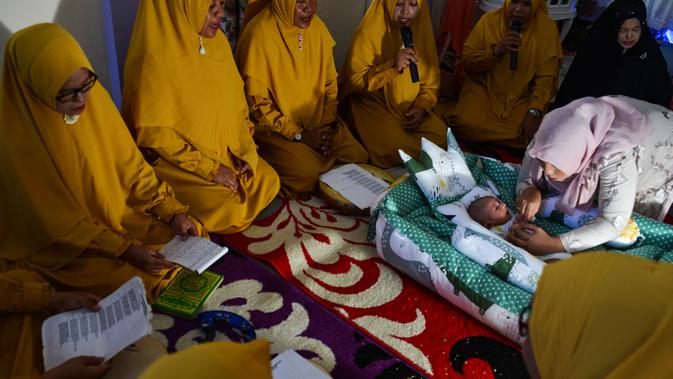 Seorang ibu memegang bayinya saat ritual 'peutron tanoh aneuk' (turun tanah anak) di Banda Aceh, Aceh, Senin (15/7/2019). Ritual turun tanah anak telah menjadi tradisi sakral bagi masyarakat Aceh yang dilaksanakan pada saat bayi berusia 44 hari. (CHAIDEER MAHYUDDIN / AFP)