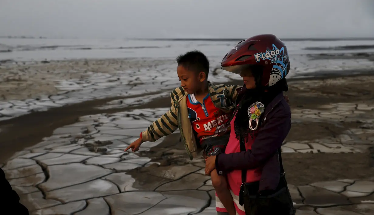 Seorang wanita menggendong anaknya saat mereka berdiri di atas lumpur kering Lapindo di Sidoarjo, Jawa Timur, 11 Oktober 2015. Beberapa tahun silam, Porong didera bencana, namun kini kawasan tersebut malah jadi objek wisata tak biasa. (REUTERS/Beawiharta)