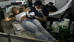 Seorang seniman saat menato seorang perempuan dibagian perutnya saat Festival Internasional Tattoo Week Rio 2016 ketiga di Rio de Janeiro, Brasil, (22/1/2016). (REUTERS/Pilar Olivares)